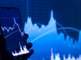 Source: https://unsplash.com/photos/a-person-holding-a-cell-phone-in-front-of-a-stock-chart- K5mPtONmpHM